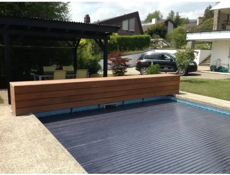 AquaTop-Poolabdeckung mit Aufrollvorrichtung über dem Wasserspiegel – 60 x 14 mm, dunkelblaue gerippte Oberfläche, Holzbank daneben