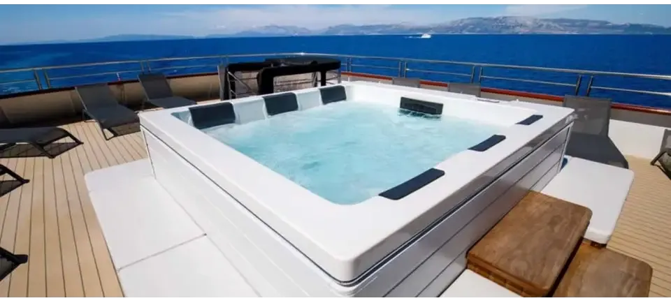PassionSpa Serene 6 Fire Pit Whirlpool – weiße Ausführung, rechteckige Form, schwarze Paneele, klares blaues Wasser, Holzterrasse