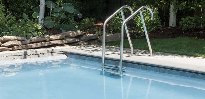 Poolleiter aus Edelstahl – eine Stufe und gebogene Handläufe, am Pool, klares blaues Wasser