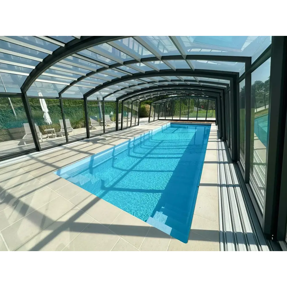 Lång rektangulär glasfiberpool Bahama med klart blått vatten, transparent glastak och svart metallram