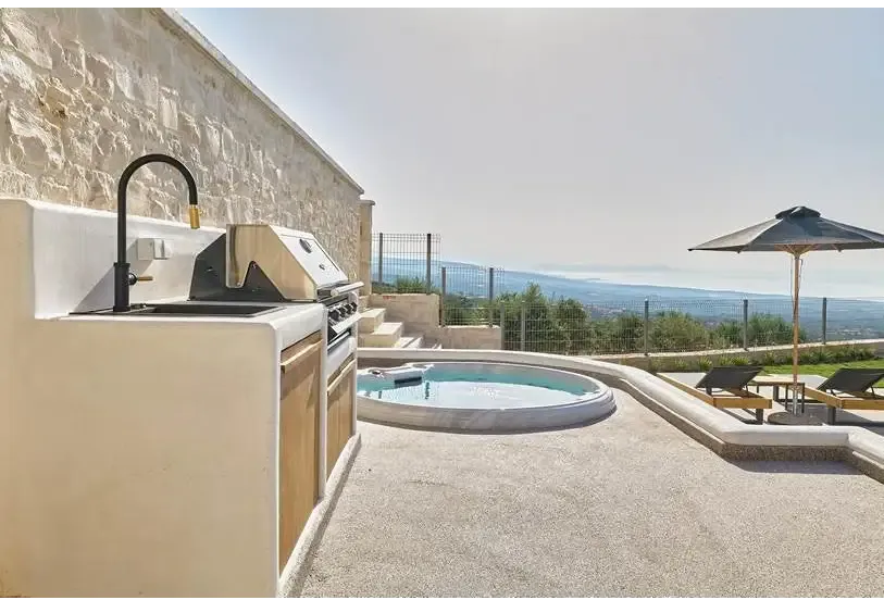 PassionSpa Recharge Whirlpool – Pure Collection, Außenküche aus beigem Stein mit schwarzer Armatur und Edelstahlgrill
