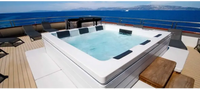 PassionSpa Serene 6 Fire Pit Whirlpool – weiße Ausführung, rechteckige Form, schwarze Paneele, klares blaues Wasser, Holzterrasse