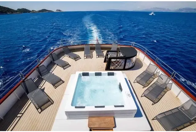 PassionSpa Serene 6 Whirlpool – weiße Ausführung, Feuerstelle, rechteckige Form, klares blaues Wasser, schwarzer Rand, auf einem Bootsdeck