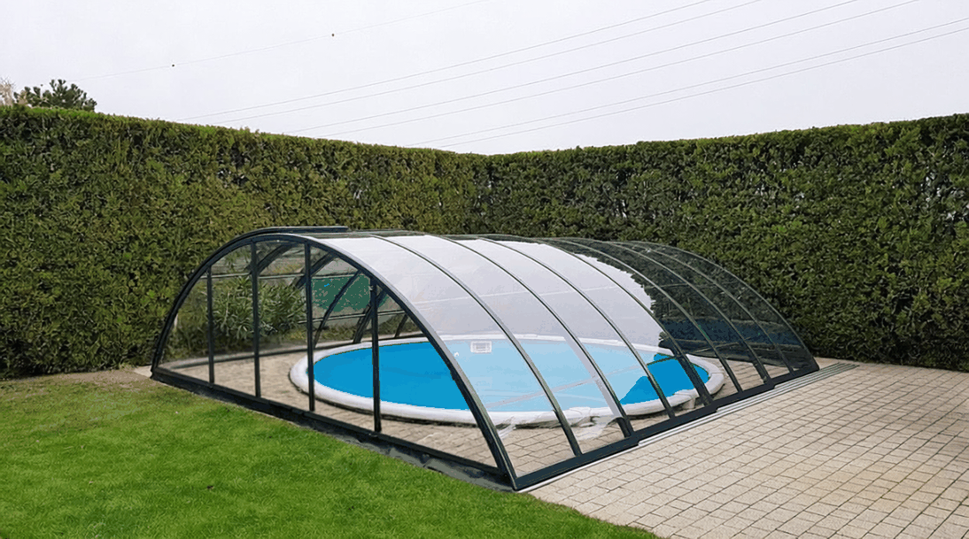 Anthrazitfarbene Classic Poolüberdachung mit gewölbter Form und klaren Polycarbonatflächen im Garten.
