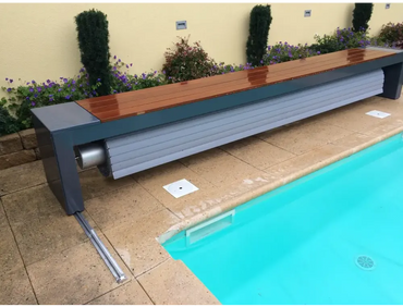 TopMoov-Lamellenabdeckung mit oberirdischer Aufrollvorrichtung – modernes Design, Bank am Pool, Lamellen mit 60 x 14 mm, Holz und graues Metall